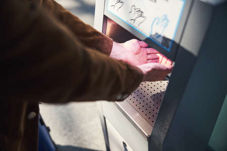 Young man using automatic hand sanitizer at airportの写真素材
