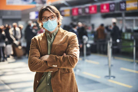 Stylish young man in protective face mask standing at airport