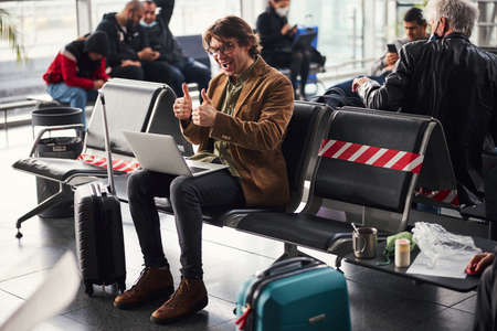 Cheerful young man using laptop in departure loungeの写真素材