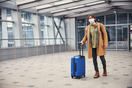 Stylish man in medical mask standing in airport terminalの写真素材