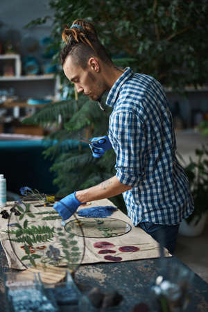Bearded male herbalist masking herbarium in workshop