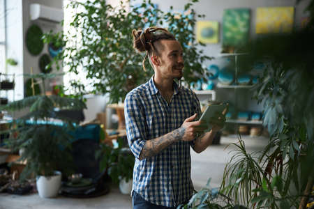 Cheerful man holding digital tablet computer and checking plants
