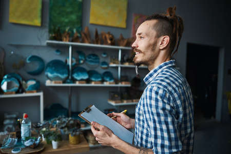 Cheerful young man with clipboard standing in workshopの写真素材