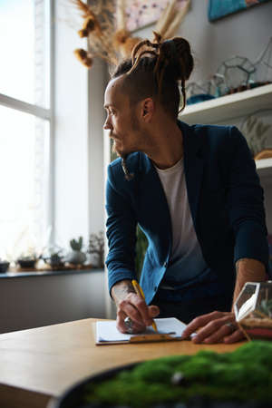 Stylish young man writing on clipboard at homeの写真素材