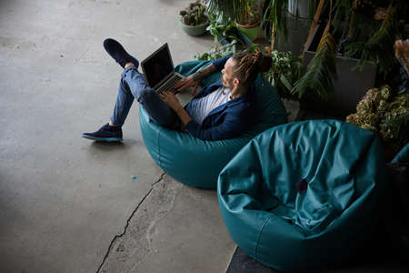 Handsome gentleman sitting on beanbag chair and working on modern notebook