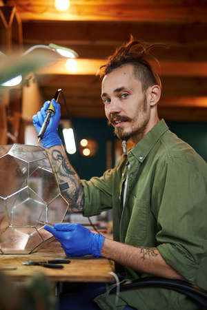 Joyful young man making glass florarium in workshopの写真素材