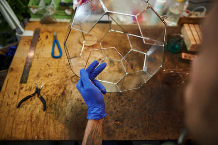 Close up of male person in sterile gloves sitting at the table and holding piece of glass while making container for plantsの写真素材