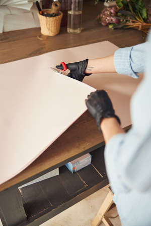 Skilled florist in nitrile gloves scissoring up the wrapping materialの写真素材