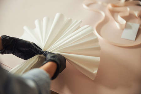 Floral designer in gloved hands folding a paper fan