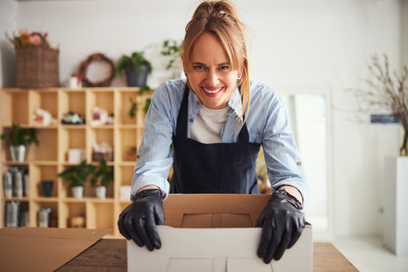 Merry floral designer leaning on an open cardboard boxの写真素材