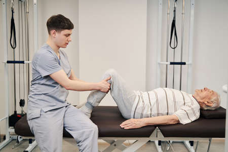 Physiotherapist doing therapeutic exercise on couch with his patient