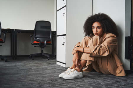 Upset young woman sitting by the office cabinetの写真素材