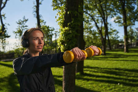 Merry female exercising with dumbbells in sunny parkの写真素材