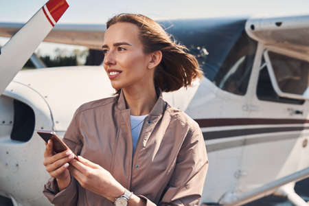 Charming young woman using mobile phone at airportの写真素材