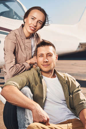 Beautiful young couple sitting near aircraft at airfieldの写真素材