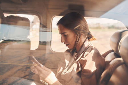 Charming young woman using smartphone in aircraftの写真素材