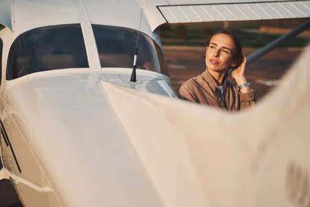 Beautiful young woman standing near airplane at airdrome