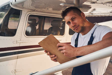 Male worker with clipboard standing near plane at airdromeの写真素材