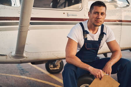 Male worker with clipboard sitting on aircraft wheel