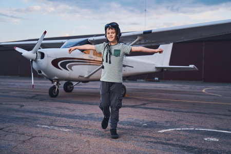 Joyful boy in aviation hat walking outdoors at aerodrome
