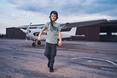 Adorable boy in aviation hat walking outdoors at aerodromeの写真素材