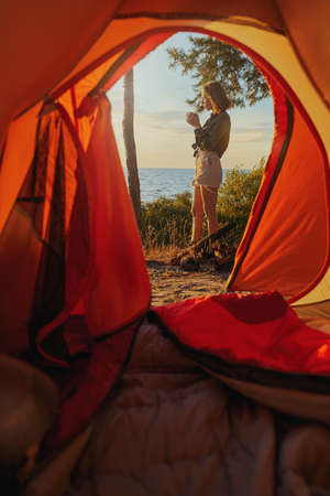 Backpacker having a drink in front of her tent