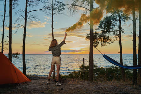 Woman in forest is waving smoke flare