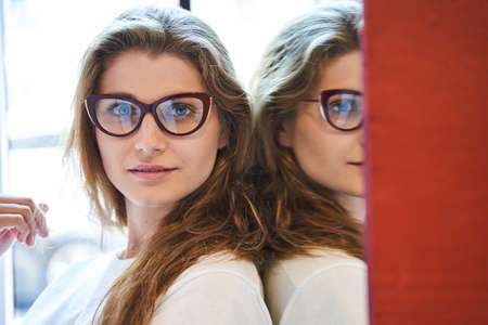 Attractive young woman in glasses standing by mirror