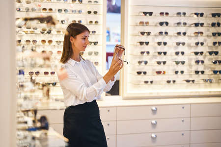 Charming young woman looking at glasses in optical storeの写真素材