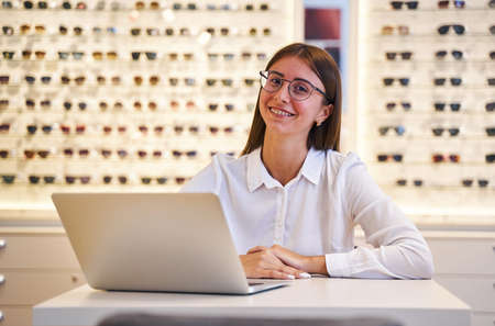Cheerful young woman using laptop in optical store