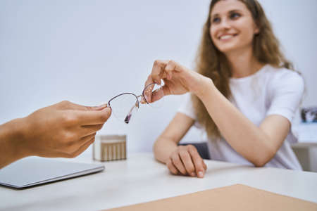 Optician giving eyeglasses to young woman in clinicの写真素材