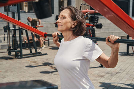 Jolly elderly female enjoying workout on sports ground