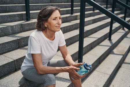 Calm active mature woman relaxing on stairs outdoorsの写真素材