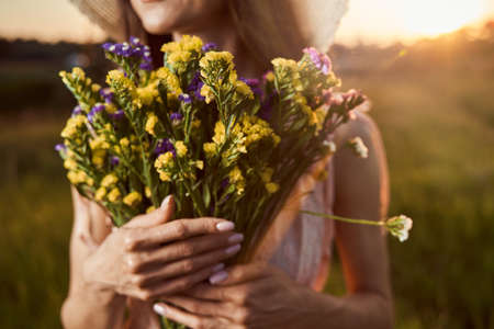 Purple and yellow flowers in hands of young womanの写真素材