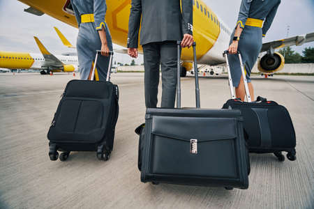 Pilot and stewardesses with luggage walking towards the landed aircraftの写真素材