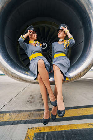 Cheerful stewardesses in pilot caps sitting cross-legged in the aeroengineの写真素材