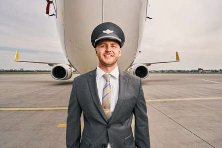 Contented stylish airline captain standing by a landed planeの写真素材