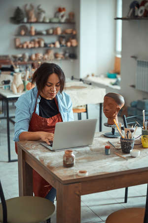 Charming female ceramist using laptop in pottery workshopの写真素材