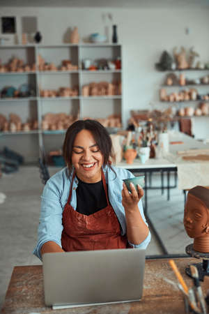 Joyful female potter using notebook in pottery workshop