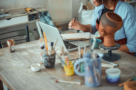 Female potter using notebook and taking notes in pottery workshopの写真素材