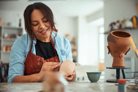 Cheerful female potter sanding clay pot in pottery workshopの写真素材