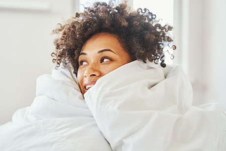 Joyous curly-haired attractive female daydreaming in bedの写真素材