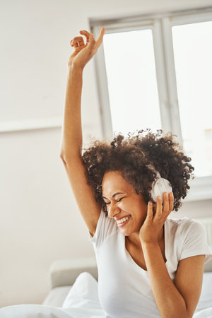 Joyful female in wireless headphones sitting in the bedroomの写真素材