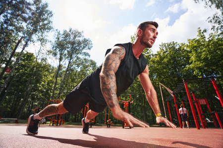 Handsome bodybuilder doing core workout on sportsground