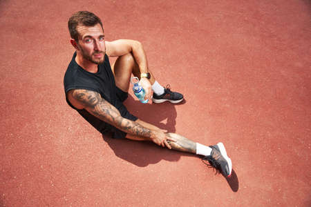 Relaxed muscular male drinking water on sportsgroundの写真素材