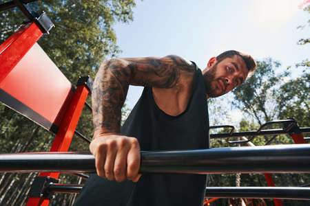 Calm tattoed bodybuilder doing push ups outdoors