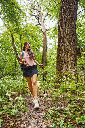 Pretty calm woman doing nordic walking in wood