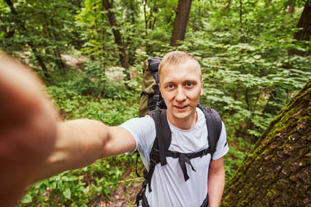 Cheerful guy taking selfie in green forest