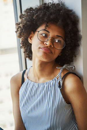 Cute calm lady in circle eyeglasses sitting by the window