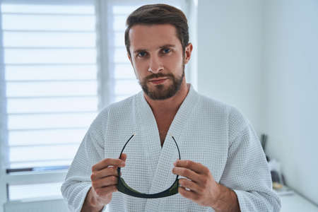 Patient with protective eyeglasses in his hands looking ahead